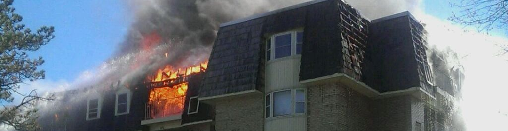 A picture of the top floor of an apartment building on fire that is being extinguished with water.